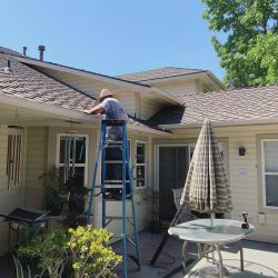 man on ladder cleaning gutter